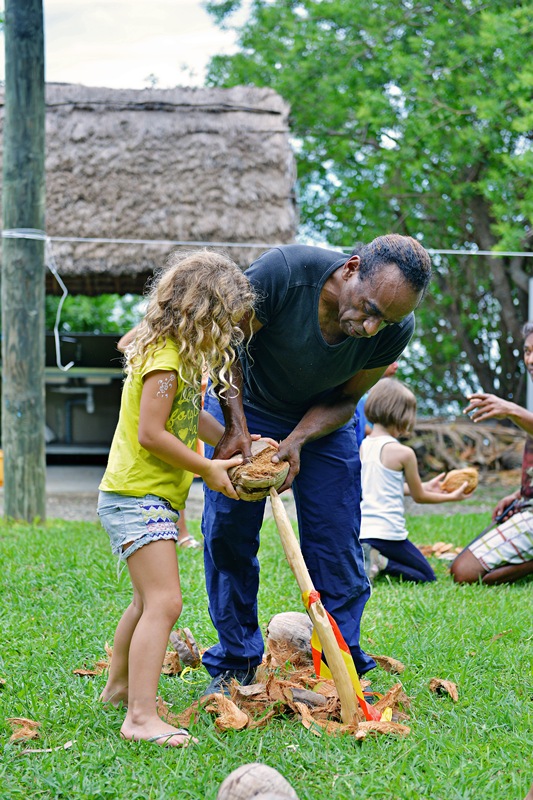 Un homme kanak et une enfant blonde ouvrent une noix de coco lors d'un atelier au Centre Culturel Djibaou Nouméa